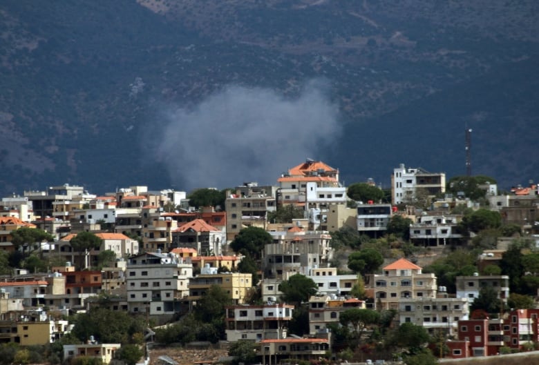 Smoke is shown in the sky and in front of mountains, behind a community of houses.