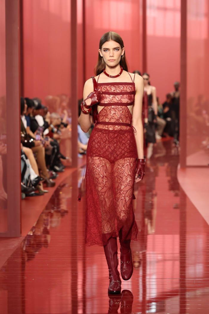 A model on a red catwalk wears a long lace slip over red shorts and boots