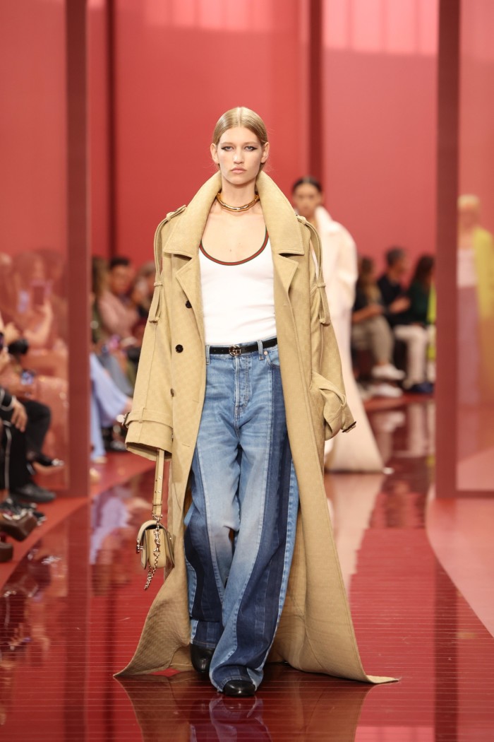 A model on a red catwalk wears an oversized coat over over-long trousers