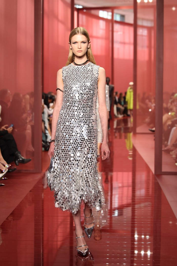 A model on a red catwalk wears a silvery sleeveless dress