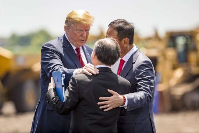 Three men in suits stand in a huddle. Donald Trump places a hand on Son’s shoulder. The other man has his arm around Son’s back