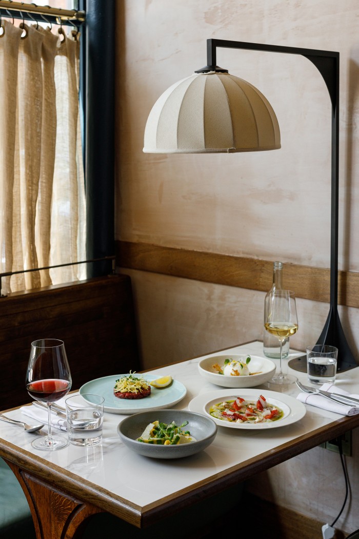 A dining setup in a restaurant with a selection of plated gourmet dishes, wine glasses, and a glass of water. A stylish beige dome-shaped lamp hangs above the table