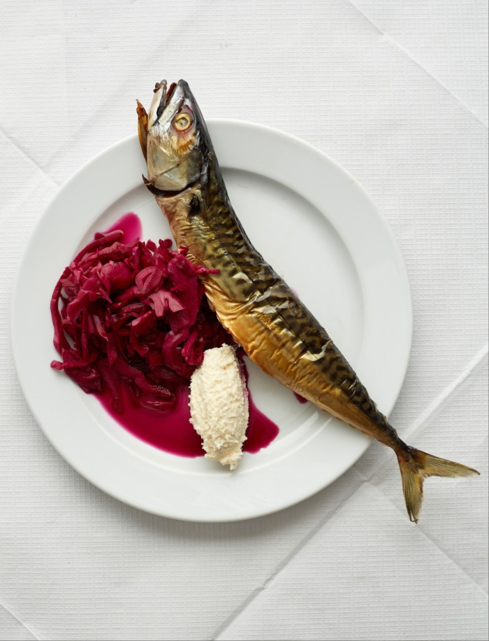 A plated dish featuring a whole smoked fish, served alongside a portion of vibrant red cabbage and a dollop of white horseradish cream