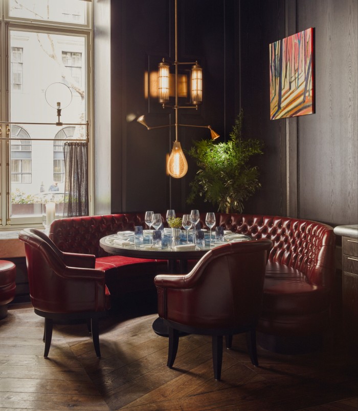 A cozy dining nook with red leather chairs and booth seating around a circular table, set with wine glasses and tableware