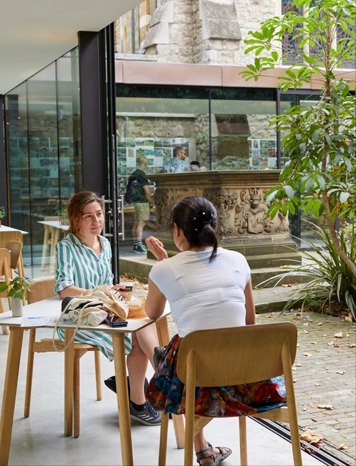 A café scene where two women engage in conversation at a table by large windows