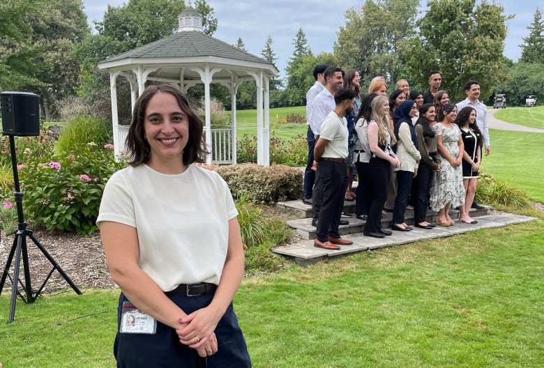 A woman in dark pants and a white shirts poses for a photo while a group of people stands in the background.