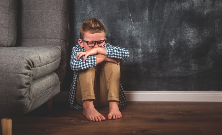 A stock image of a child sitting in a corner by a couch