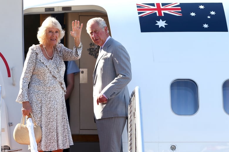 Two people stand at the tops of stairs before boarding an airplane that has the Australian flag displayed on it.