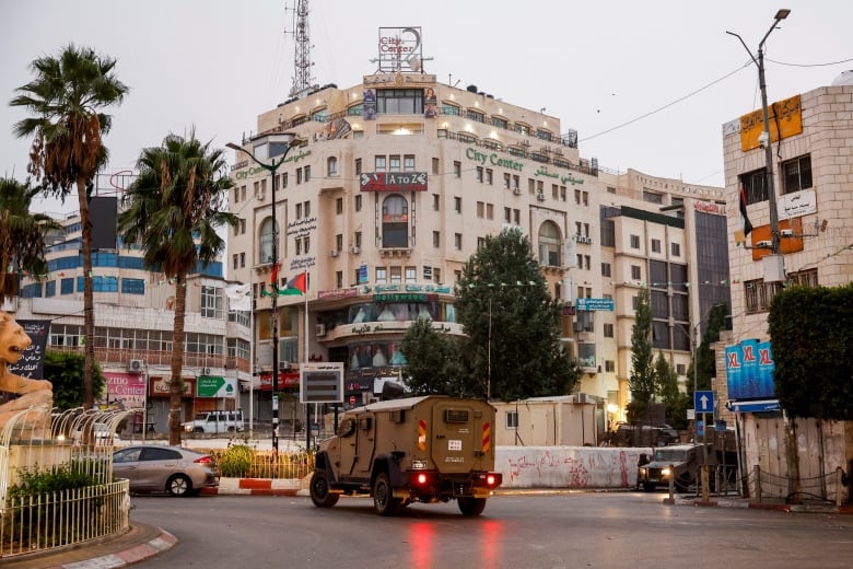 A military vehicle moves in a street outside a building.