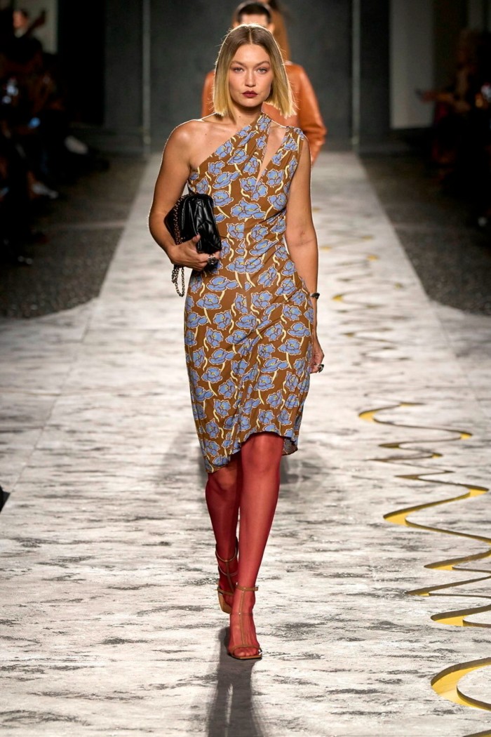 A female catwalk model wearing a patterned dress and red stockings