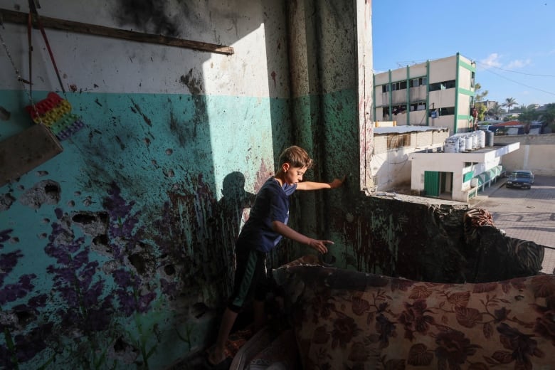 A young boy looks at damaged concrete inside a building.