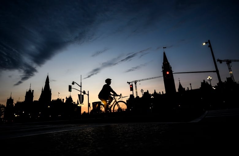 A cyclist rides past Parliament Hill, along Ottawa's Wellington Street, as the sun sets.