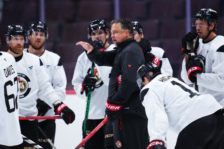 A male ice hockey coach addresses his team on the ice during practice.