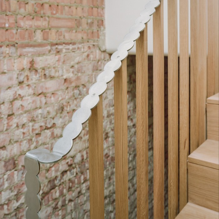 A wooden staircase, where the wooden banisters are topped with a bespoke metal handrail