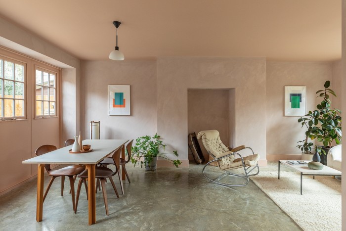 A large room decorated in neutral colours. On the left, is a dining area featuring a table with wooden legs and a white top. On the right, a sitting area, with a modern rocking chair and coffee table