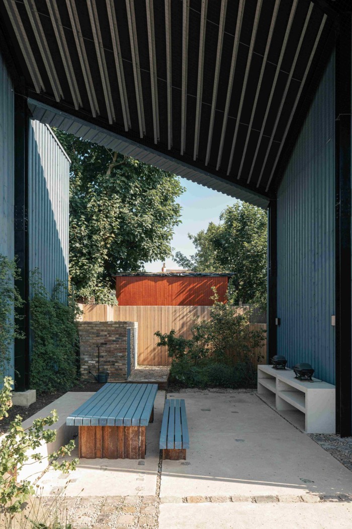 An outside seating area between two walls, with a roof above. There is a low wooden table and bench, both painted blue.