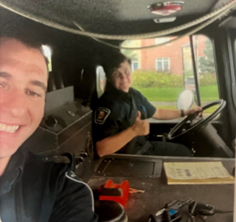 Two firefighters sit in a fire truck cab and smile in this grainy selfie.