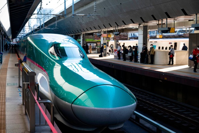 A train with a heavily elongated turquoise-coloured nose cone in a train station