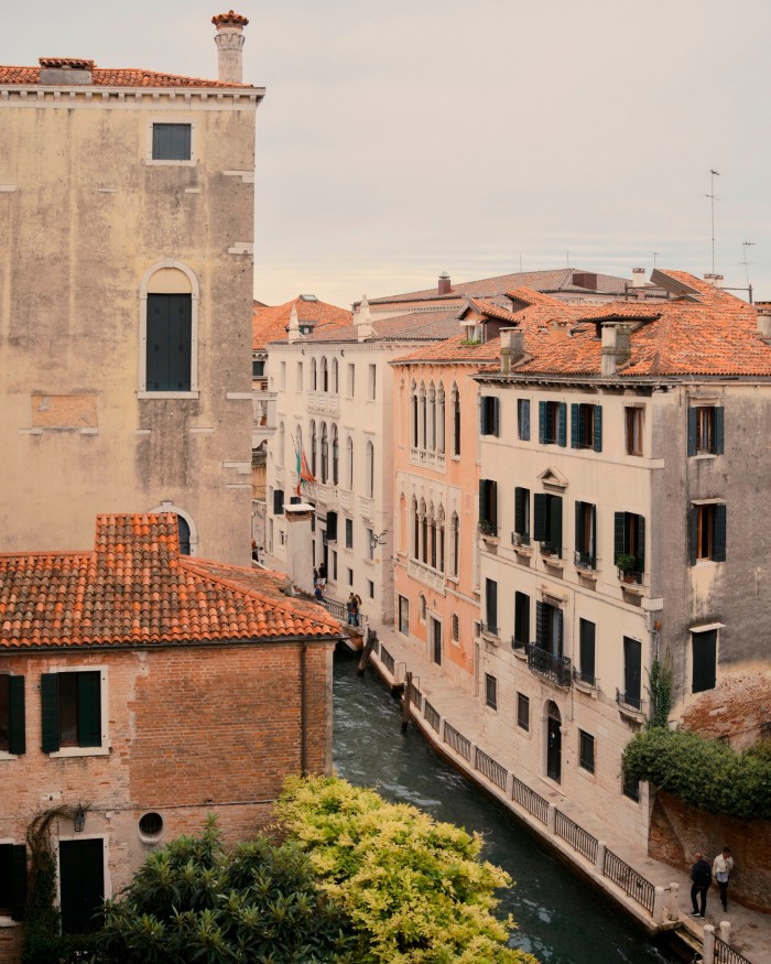 Typical, terracotta-roofed Venetian houses and areas of greenery are seen either side of a canal 