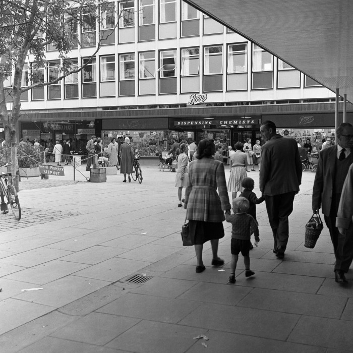 A black and white photo of families out shopping in pedestrianised streets of functional late 1950s architecture