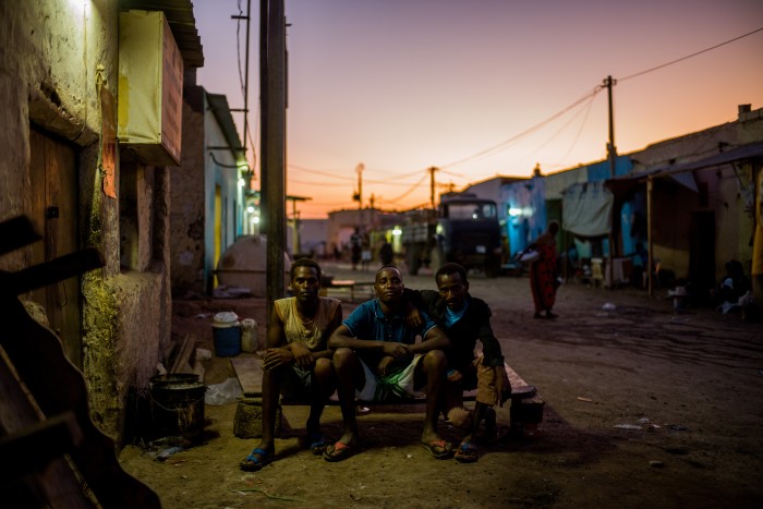 Three Ethiopian tahrib settle themselves on the wooden bench of a vacated tea stall