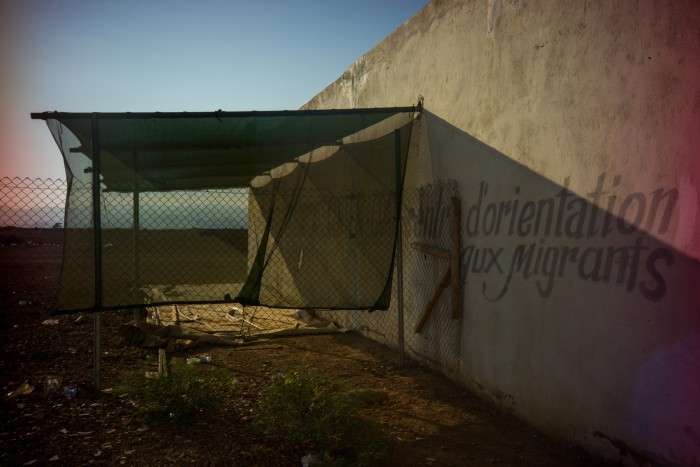 A sun shade for new arrivals overhangs a wall signed d’orientation aux migrants at a reception centre run by the International Organization for Migration