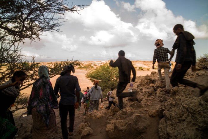 A group of people walking through a rocky, arid landscape with trees and sparse vegetation