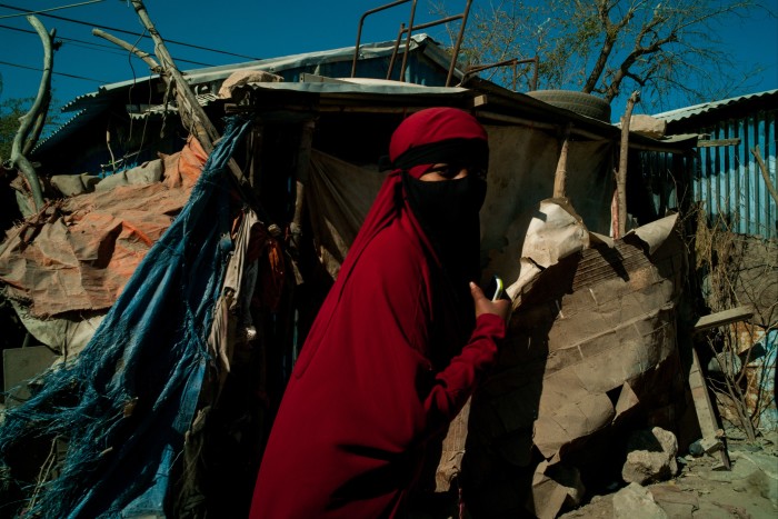 Wearing a nib over a red Somali jilbab, a Yemeni woman walks past shelters built of sheet iron, wood and plastic sheeting