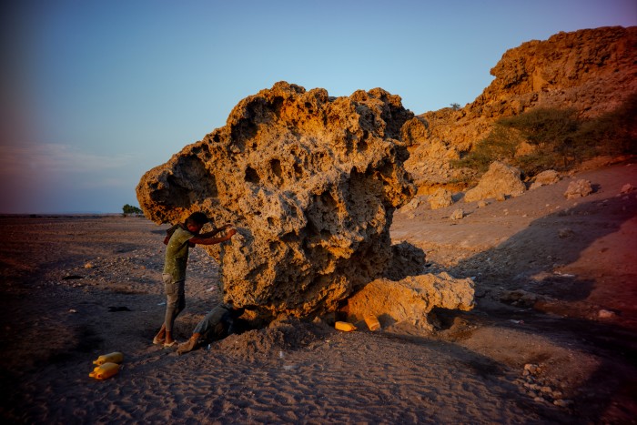 A person standing next to a large, weathered rock formation in a desert-like landscape