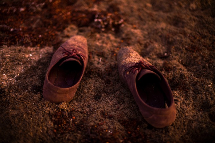 A pair of worn shoes left on the sandy ground, partially covered in dust and sand