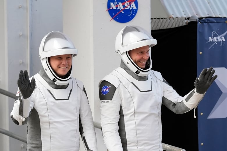 Two astronauts wave as they pose for photographs.