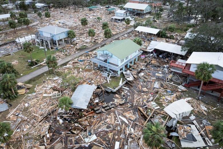 An aerial view shows a neighbourhood littered with debris and populated by damaged homes.