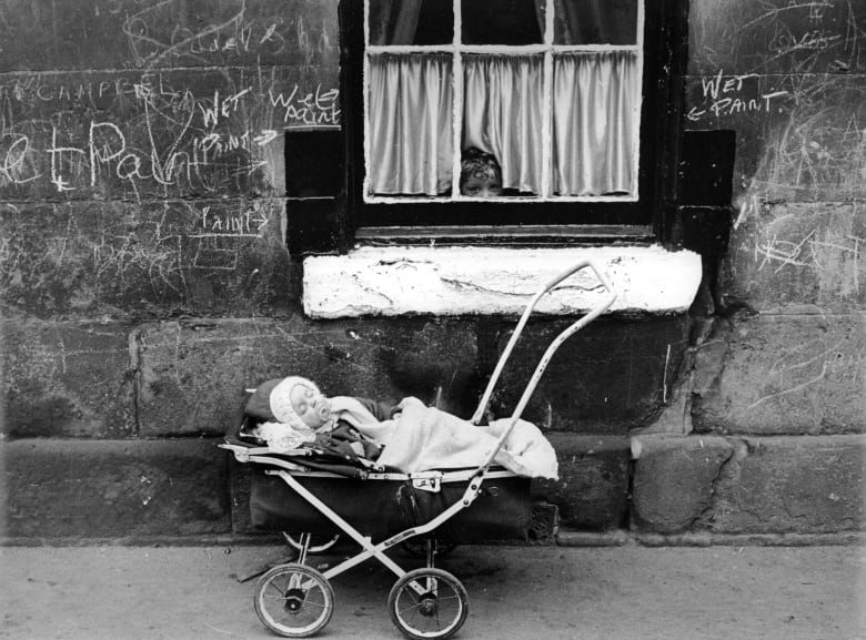 A child looks at a baby in a pram from the window of a tenement block