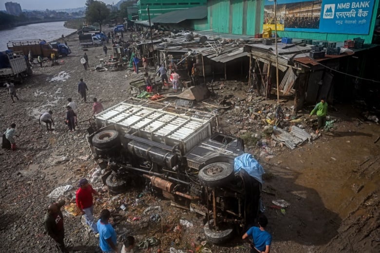 A damaged vehicle lies amid mud and debris in a flood-affected area. 