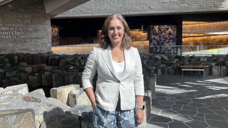 Woman stands in beige blazer and smiles at camera