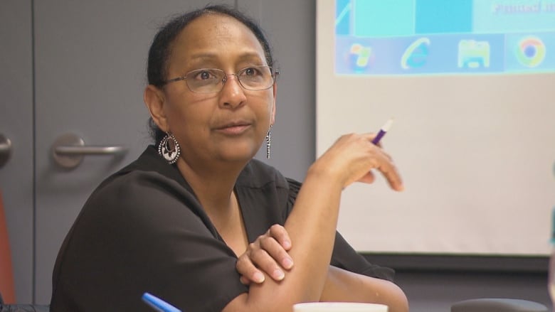 A woman sits at a table holding a pen