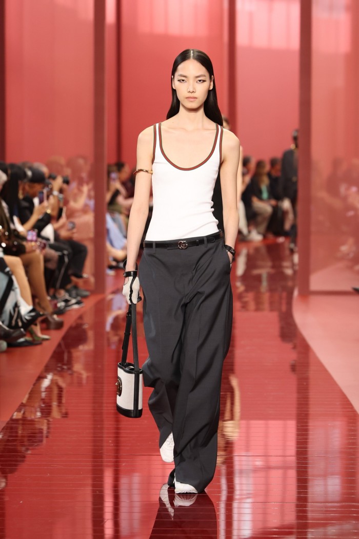 A slim female catwalk model wearing a white singlet with dark wide suit trousers