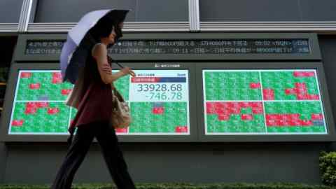 A woman walks in front of an electronic quotation board displaying the numbers of share price on the Tokyo Stock Exchange