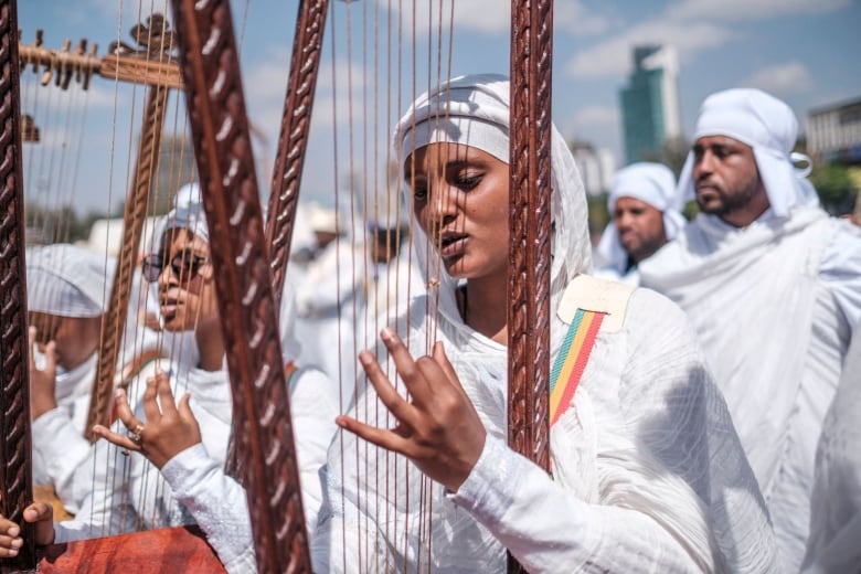 A woman in a white robe and head covering plays the harp in an orchestra 