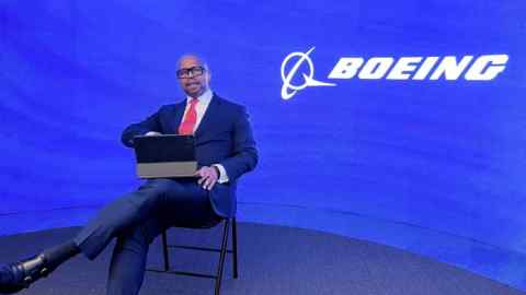 Ted Colbert seated with a laptop on his lap with a Boeing logo on the wall behind him