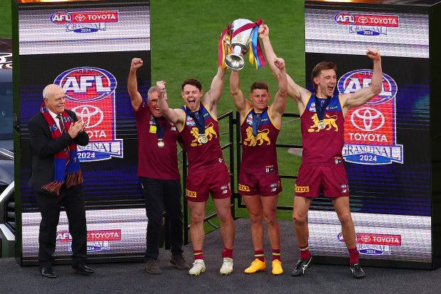 Leigh Matthews watches on as Chris Fagan, Lachie Neale, Dayne Zorko and Harris Andrews lift the 2024 premiership cup.