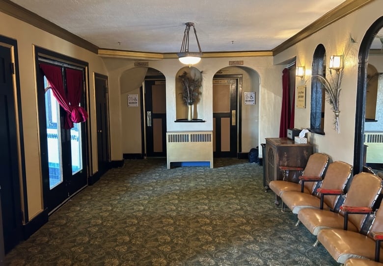 A small lobby space is decorated with gold trim and patterned carpeting, with old movie seating installed along one wall. 