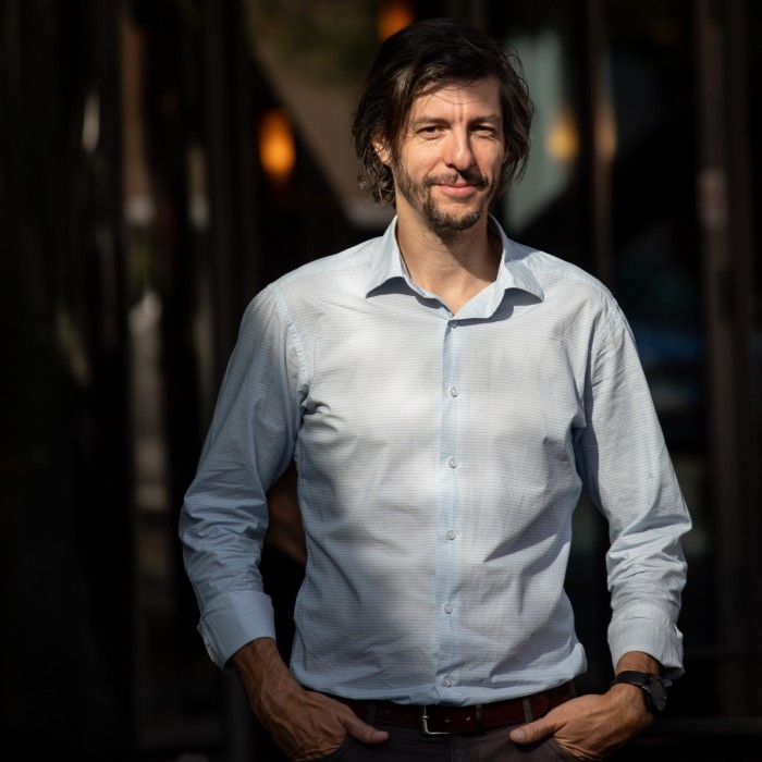 Radek Hábl is posing outdoors in Prague wearing a light blue shirt with his hands in his pockets