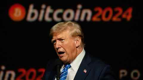 A man in a suit speaks on stage with a Bitcoin 2024 banner in the background