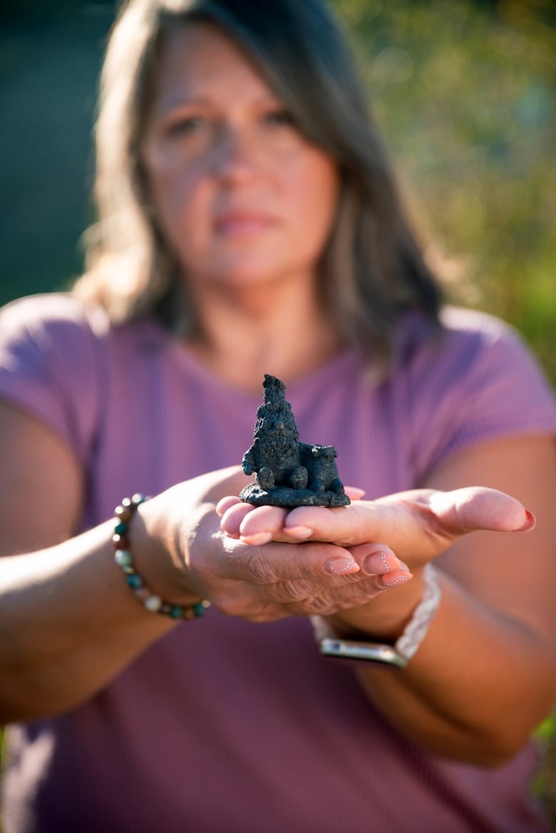 A woman holds a blackened gnome in her hand.