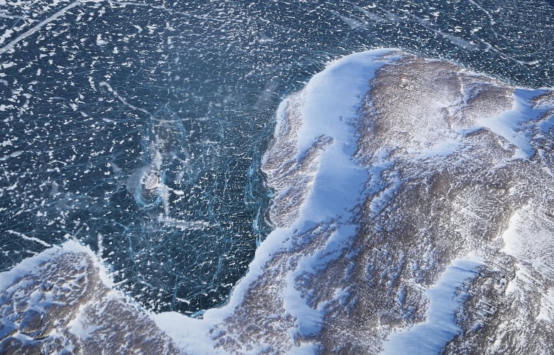 An aerial photo looking down at a part of Greenland where dark blue water curves around an icy landscape.