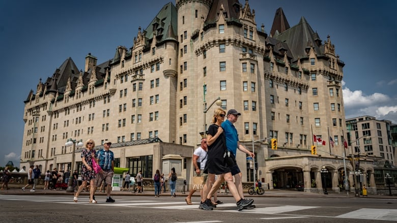 People walking on the sidewalk in front of a grand hotel. 