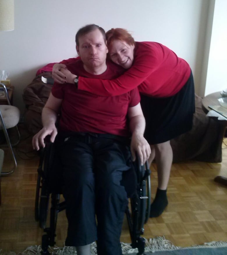 A smiling woman hugs a man sitting in a wheelchair.