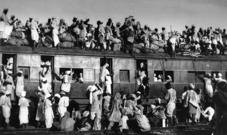 Black and white photo of huge crowds of people on, near and on top of a train 