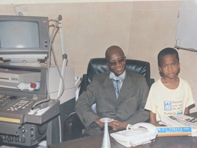 A boy looks at the camera as a man sits behind him, smiling. 